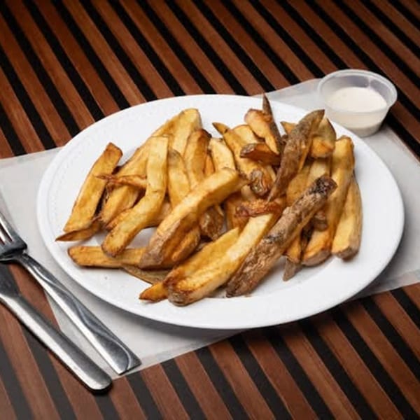 A white plate piled high with golden-brown steak fries, with a side of dipping sauce and silverware.