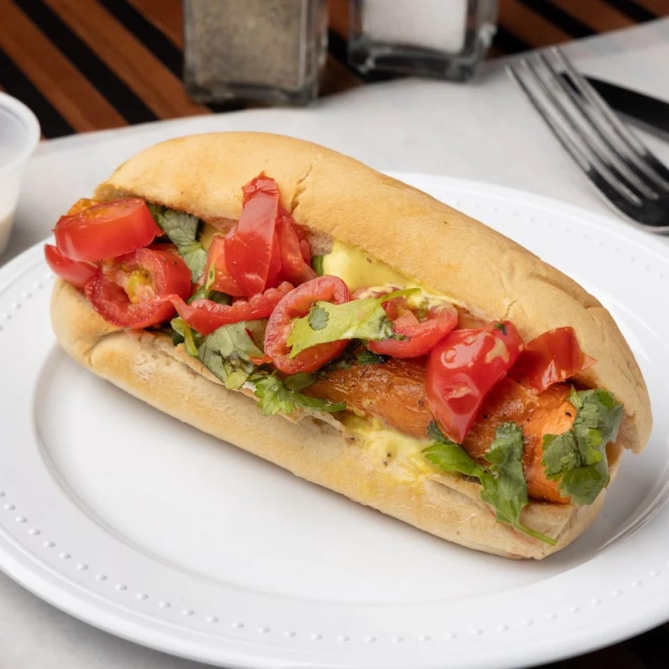 A close-up of a hot dog in a bun, topped with chopped tomatoes, cilantro, and sauce.
